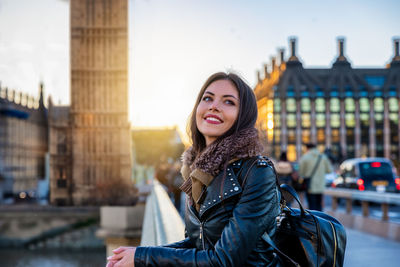 Smiling young woman looking away while standing in city during winter