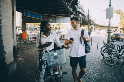 Smiling multi-ethnic friends talking while walking on sidewalk in city