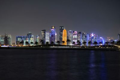 Illuminated buildings by river against sky at night