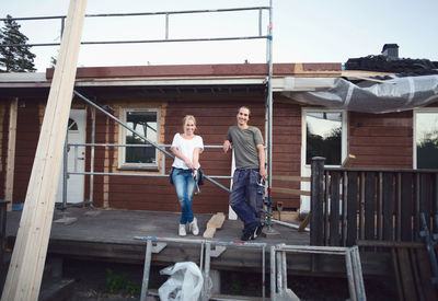 Full length portrait of happy couple leaning on scaffolding of house being renovated