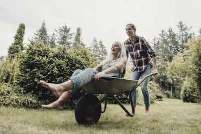 Daughter pushing mother, sitting in push cart, through the garden