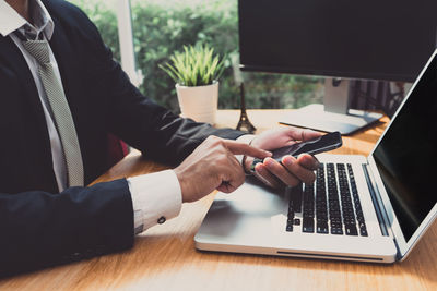 Midsection of businessman using phone by laptop on table