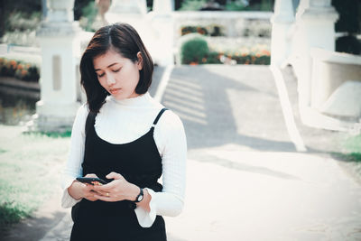 Woman looking using mobile phone while standing outdoors