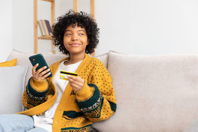 Young woman using mobile phone while sitting on sofa at home