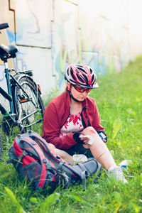 Injured female cyclist applying medicine on wound while sitting at park