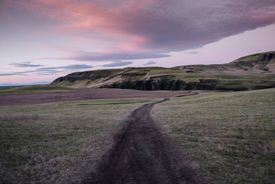 Road amidst field against sky during sunset