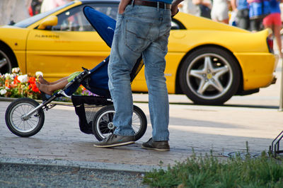 Low section of man standing by baby carriage on footpath