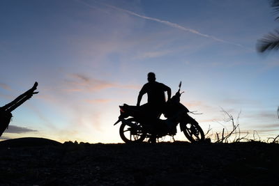 Silhouette man riding bicycle on land against sky during sunset