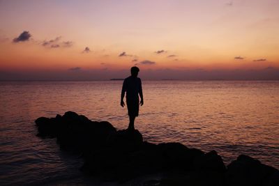 Silhouette man standing on rock by sea against sky during sunset