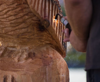 Cropped image of man using blow torch on wooden sculpture