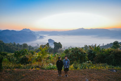 Full length of couple standing by cloudscape against sky during sunset