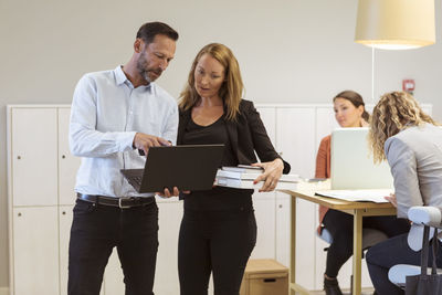 Mature businessman showing laptop to female colleague in board room