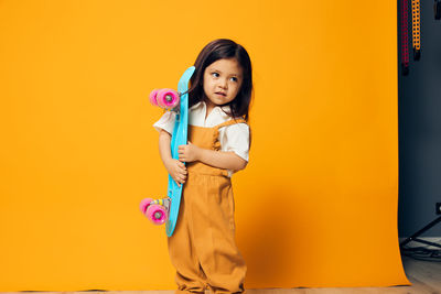 Portrait of young woman standing against yellow wall