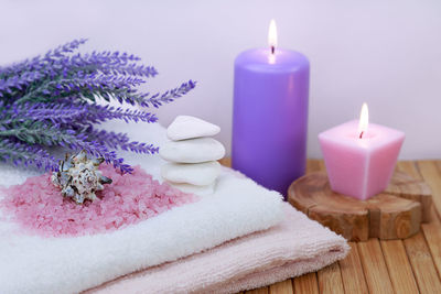 Candles with salts and flowers by towel on table