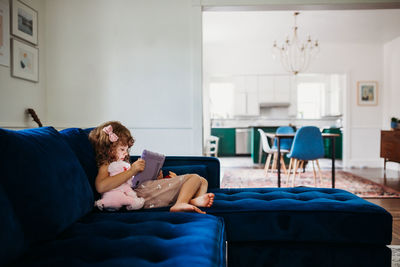 Young girl sitting on couch in modern living room learning on tablet