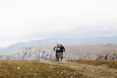 People riding bicycle on mountain against sky