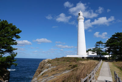 Path to the white lighthouse standing on the cliff edge under blue skies