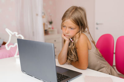 Schoolgirl looks thoughtfully at a laptop screen while distance learning
