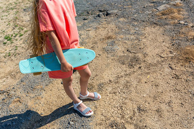 A slender teenage girl with a skateboard in her hand in a summer trendy suit.