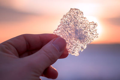 Cropped image of hand holding ice during sunset