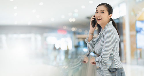 Smiling young woman using mobile phone while standing at camera