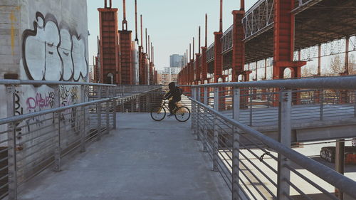 Side view of man riding bicycle on bridge against clear sky