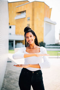 Portrait of young woman gesturing equal sign while standing against building