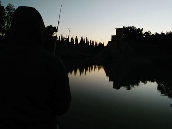 Rear view of silhouette man by lake against clear sky