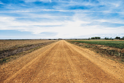 Dirt road amidst field against sky