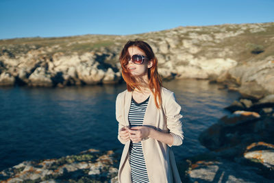 Woman wearing sunglasses standing on rock at shore