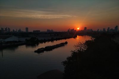 Scenic view of river by buildings against sky during sunset