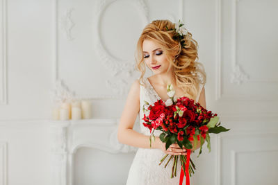 Young woman with red rose against white wall