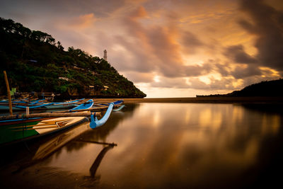 Boat moored in lake against sky during sunset