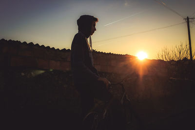 Side view of young man with bicycle against sky during sunset