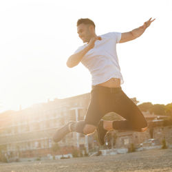 Full length of young man jumping in city against clear sky