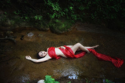 High angle view of woman wrapped with red fabric lying in stream