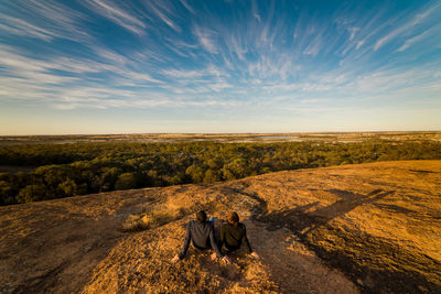 Rear view of men sitting on landscape against sky