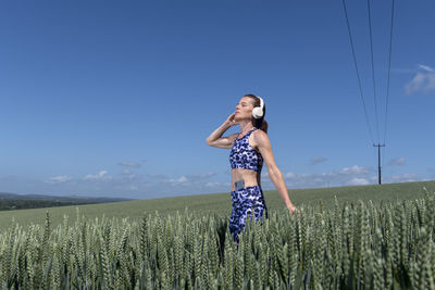 Sporty, fit woman listening to music with wireless headphones in a field.