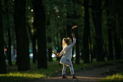 Full length of girl with hand raised standing in forest
