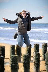 Portrait of woman with arms outstretched jumping at beach against sky