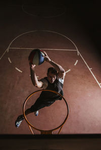 Basketball player in black and white sport clothes jumping and making dunk while training on sports ground