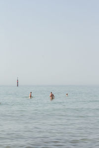 People swimming in sea against clear sky