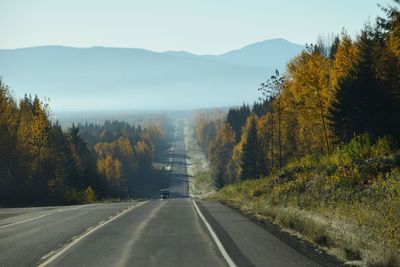 Country road amidst trees against sky