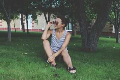 Woman wearing sunglasses while sitting on grassy field at park