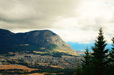 Cityscape by mountain against cloudy sky