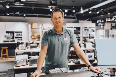 Portrait of smiling mature salesman standing at counter in electronics store