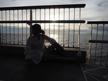 Rear view of woman sitting on railing against sea