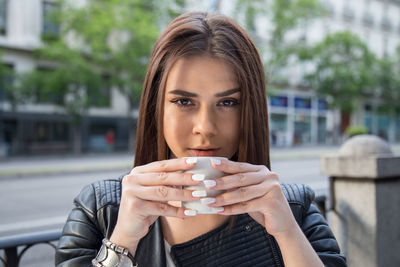 Close-up portrait of young woman drinking coffee at sidewalk cafe