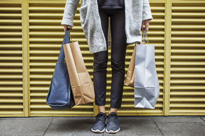 Low section of woman holding bags while standing on sidewalk