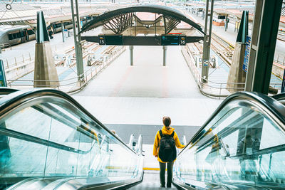 Rear view of woman walking on escalator in shopping mall